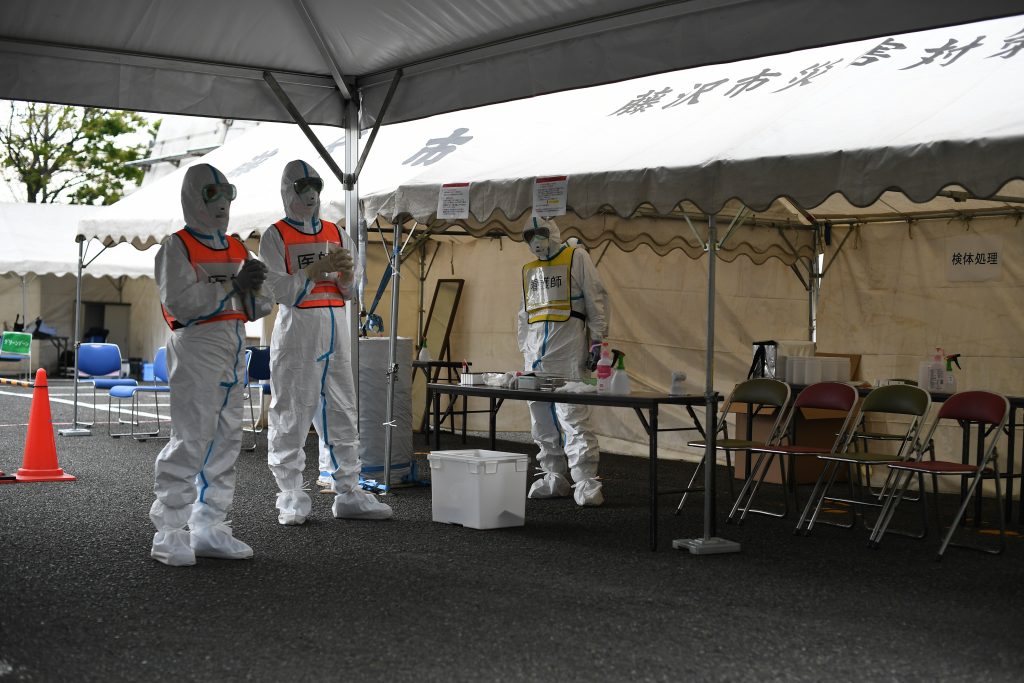 Doctors (L-in orange vests) and a nurse (R-in yellow vest) wearing protective gear stand by before a demonstration of a drive-through polymerase chain reaction (PCR) swab test for the COVID-19 coronavirus in Fujisawa in Kanagawa prefecture, southwest of Tokyo, on April 27, 2020. (AFP)