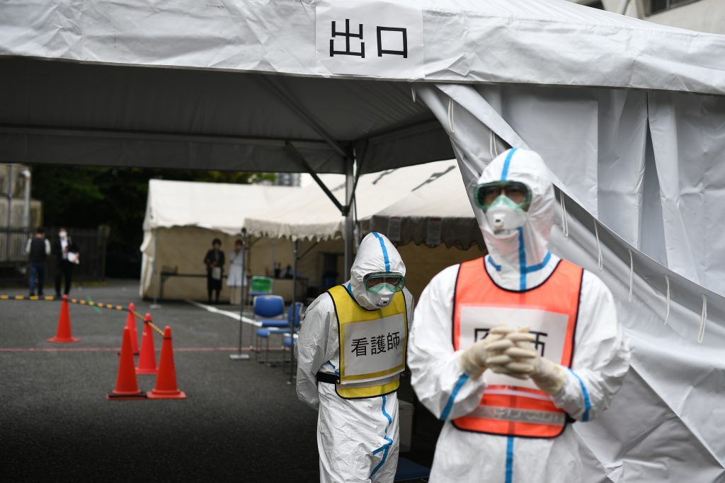 A doctor (R-in orange vest) and a nurse (C-in yellow vest) wearing protective gear stand by a PCR drive-through swab test for the COVID-19 coronavirus in Fujisawa in Kanagawa prefecture, southwest of Tokyo, on April. 27, 2020. (AFP)