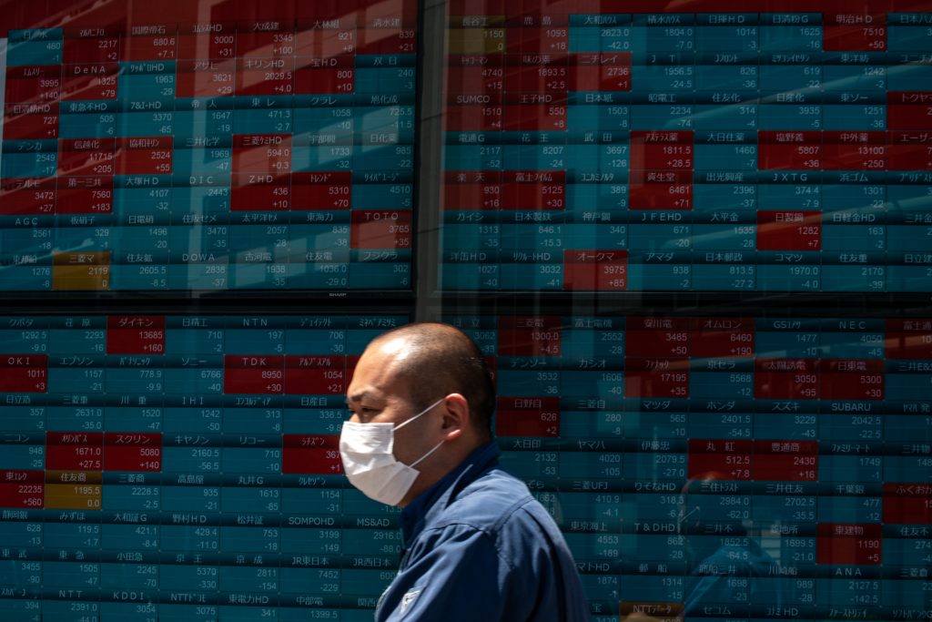 A pedestrian wearing a face mask walks past an electronic quotation board displaying stock prices in Tokyo on May 7, 2020. Tokyo stocks opened lower on May 7 after a three-day public holiday, tracking recent declines on Wall Street caused by weak economic data. (AFP)