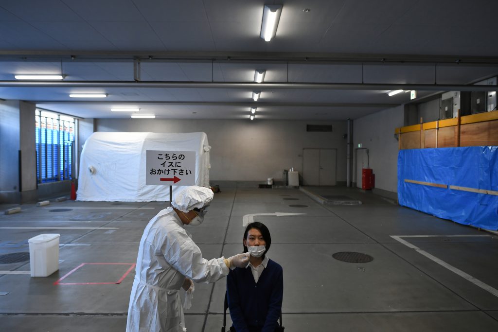 Medical staff wearing protective clothing (L) and an official acting as a patient conduct a demonstration of the polymerase chain reaction (PCR) swab test for the COVID-19 coronavirus in Tokyo on May 8, 2020. (AFP)