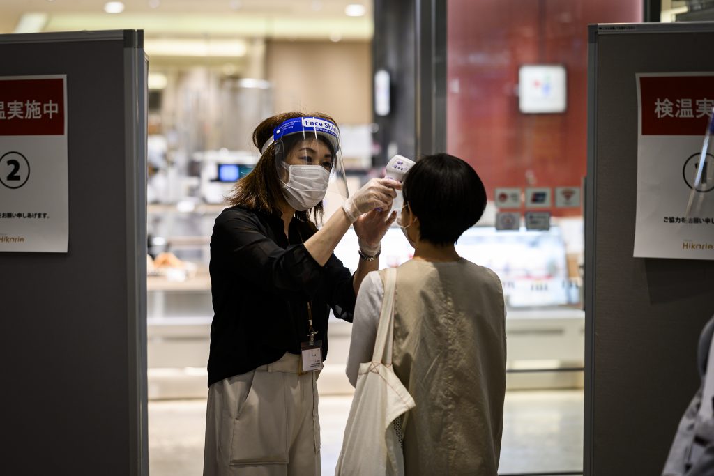 An employee wearing a mask and face shield amid concerns over the spread of the COVID-19 coronavirus conducts a temperature check on a customer at the entrance of the Shibuya Hikarie building in Tokyo on May. 26, 2020. (AFP)