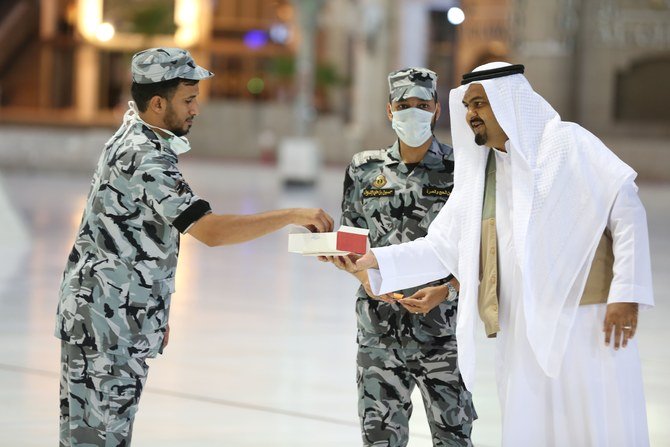 This picture taken on May 24, 2020 shows a Saudi worshipper offering sweets to a security guards, some with face masks, during Muslim Eid al-Fitr prayers at the Grand Mosque in Saudi Arabia's holy city of Makkah. (AFP)