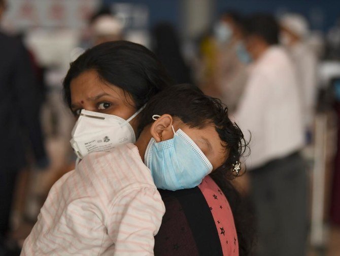 An Indian woman carries a sleeping child as she waits at the Dubai International Airport before leaving the Gulf Emirate on a flight back to her country, on May 7, 2020, amid the novel coronavirus pandemic crisis. (AFP)