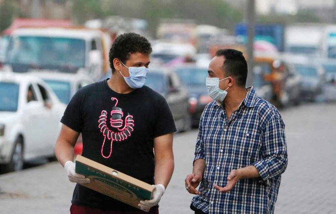 Men wearing face masks to prevent coronavirus from spreading walk along a street before curfew in Shubra El Kheima, Al-Qalyubia, north of Cairo. (Reuters)