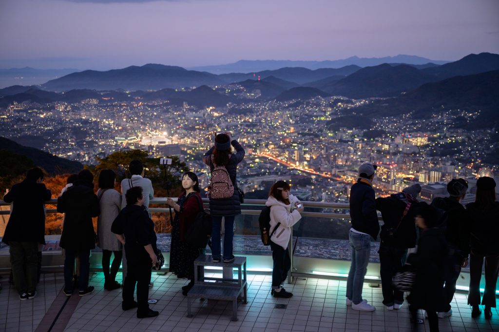 A general view shows tourists standing at a viewpoint overlooking the city skyline of Nagasaki at Mount Inasayama on November 23, 2019. (AFP)