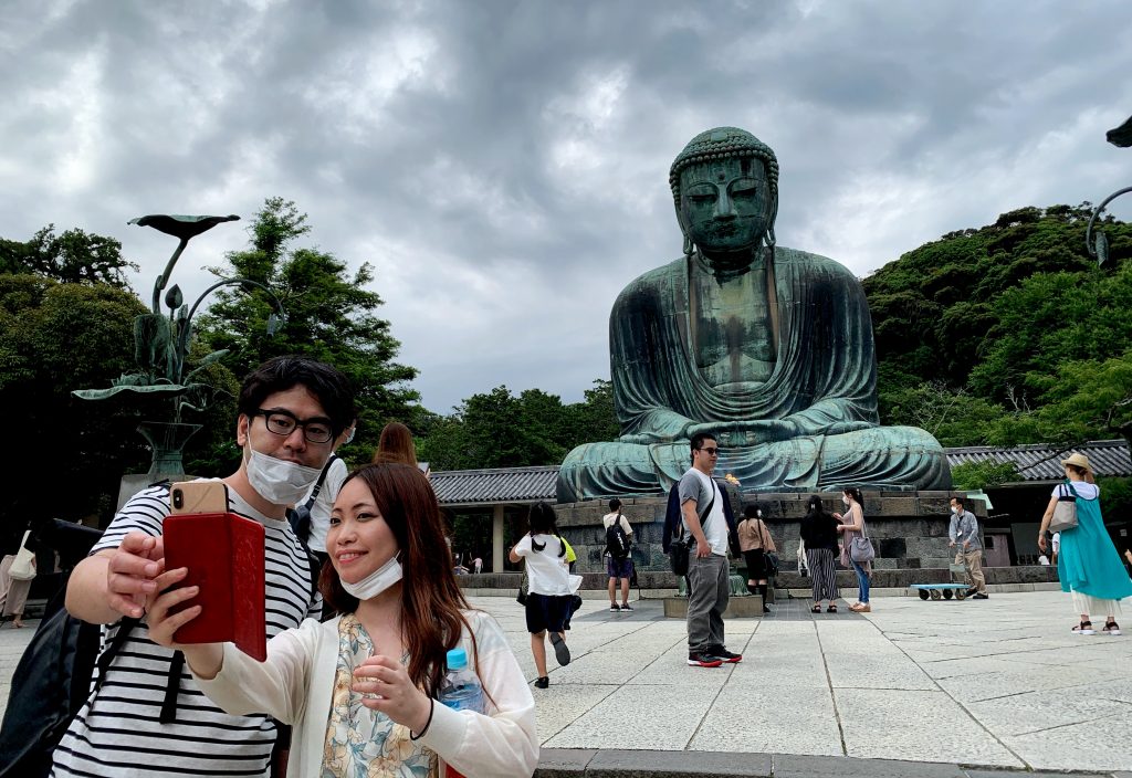 A couple wearing face masks take a selfie with the Great Buddha statue at Kotoku-in temple in Kamakura, Kanagawa prefecture on June 20, 2020. (AFP)