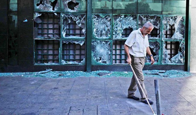 A man sweeps glass off the ground outside a bank in Lebanon’s northern port city of Tripoli after it was vandalized by protesters. (AFP)