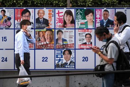This picture taken on June 26, 2020 in Tokyo shows pedestrians passing in front of a board displaying posters of candidates for the capital's gubernatorial election. (AFP)