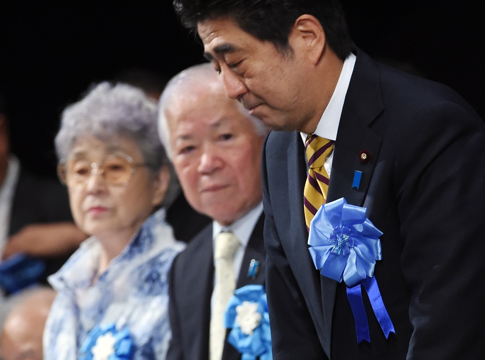 Japanese Prime Minister Shinzo Abe (right) bows to leave a rally to support families of abduction victims by North Korea as abduction victim Megumi Yokota's parents, Shigeru (center) and Sachie Yokota (left) look on in Tokyo on September 13, 2014. (AFP)