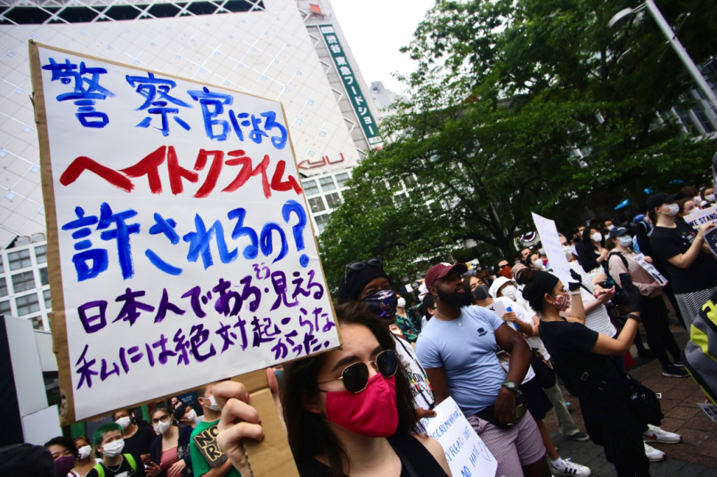 A person protesting in Tokyo holds a sign that reads “Is it allowed for the police to commit hate crimes? In Japan we don’t have such.