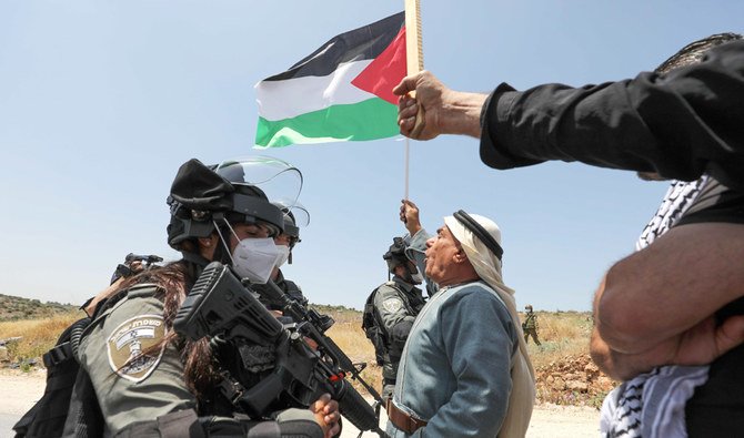 A Palestinian man facing Israeli soldiers waves a national flag during a protest against Israel's plan to annex parts of the occupied West Bank, near the town of Tulkarm on June 5, 2020. (AFP)