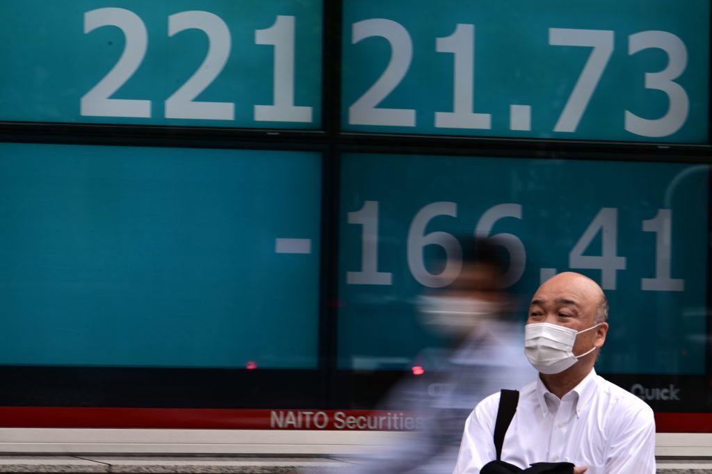 Pedestrians wearing face masks walk in front of an electric quotation board showing numbers of the Nikkei 225 index in Tokyo on July 1, 2020. (AFP)