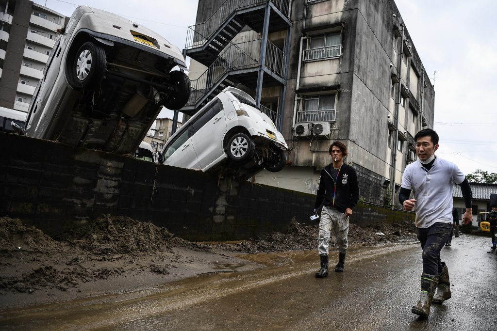 Men walk past cars upended by recent floods in Hitoyoshi, Kumamoto prefecture on July 10, 2020, after heavy rains and flooding devastated the region. (AFP)