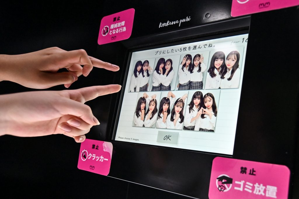 This photo taken on July 21, 2020 shows teenagers looking at images as they use a Japanese style photo booth known locally as