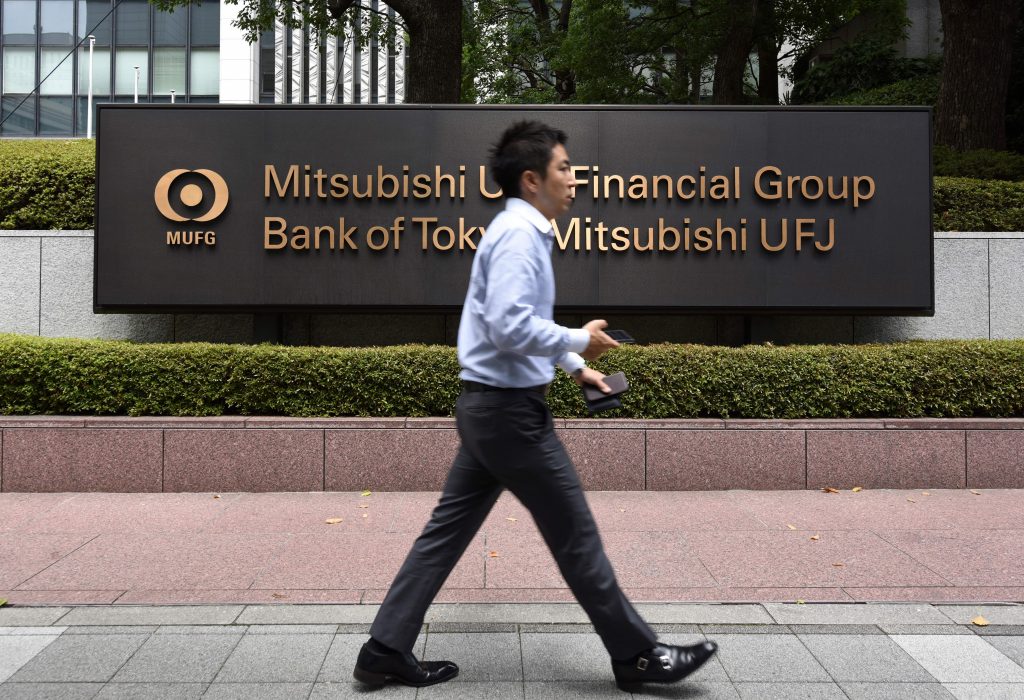 A man walks past a board of the Japanese mega bank Mitsubishi UFJ Financial Group (MUFG) in Tokyo on July 31, 2017. (AFP)
