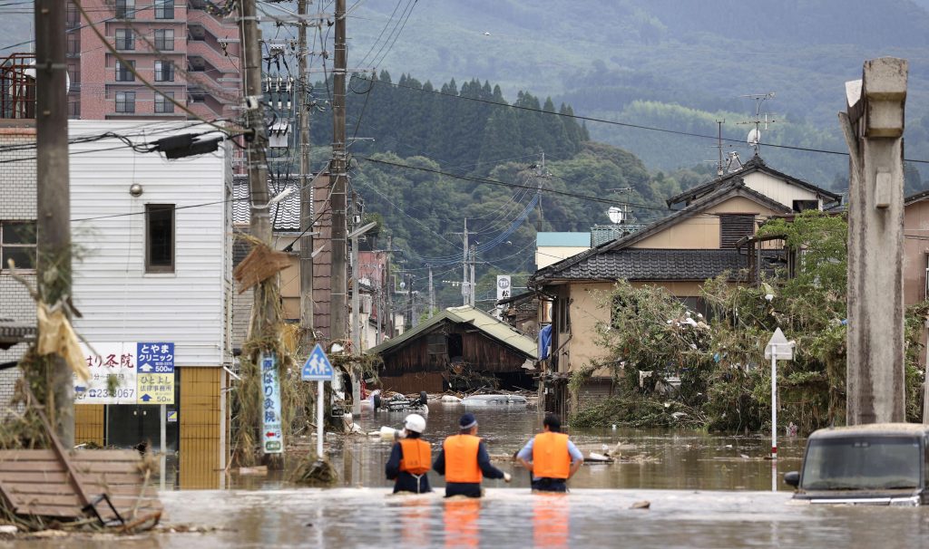 Police officers look for stranded people through a flooded street following a heavy rain in Hitoyoshi, Kumamoto prefecture, southern Japan Saturday, July 4, 2020. Heavy rain in southern Japan triggered flooding and mudslides on Saturday, leaving more than a dozen people presumed dead, some missing and dozens stranded on rooftops waiting to be rescued, officials and news reports said. (Takumi Sato/Kyodo News via AP)