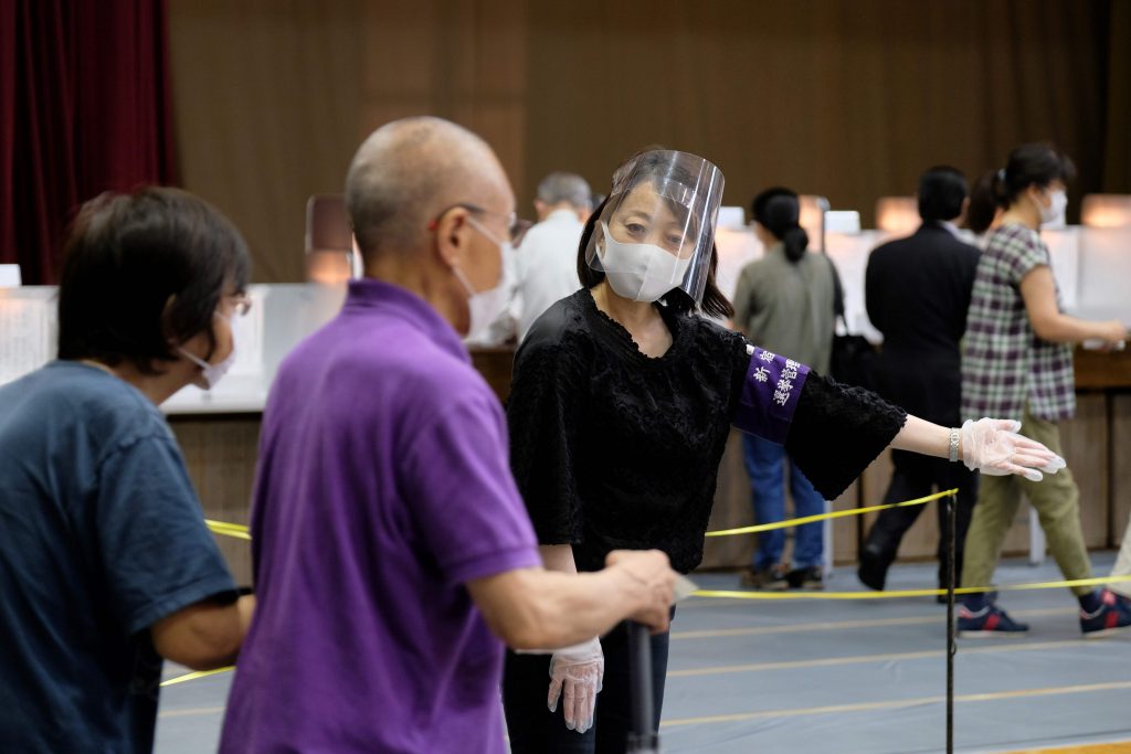 A polling station staff wearing a face mask and a face shield help voters upon their arrival at a polling station for Tokyo gubernatorial election in Shinjuku, Tokyo on July 5, 2020. The postponed Olympics and a worrying second surge in coronavirus cases are the main issues as Tokyo voters vote for governor to run one of the world's most populous cities. (AFP) 