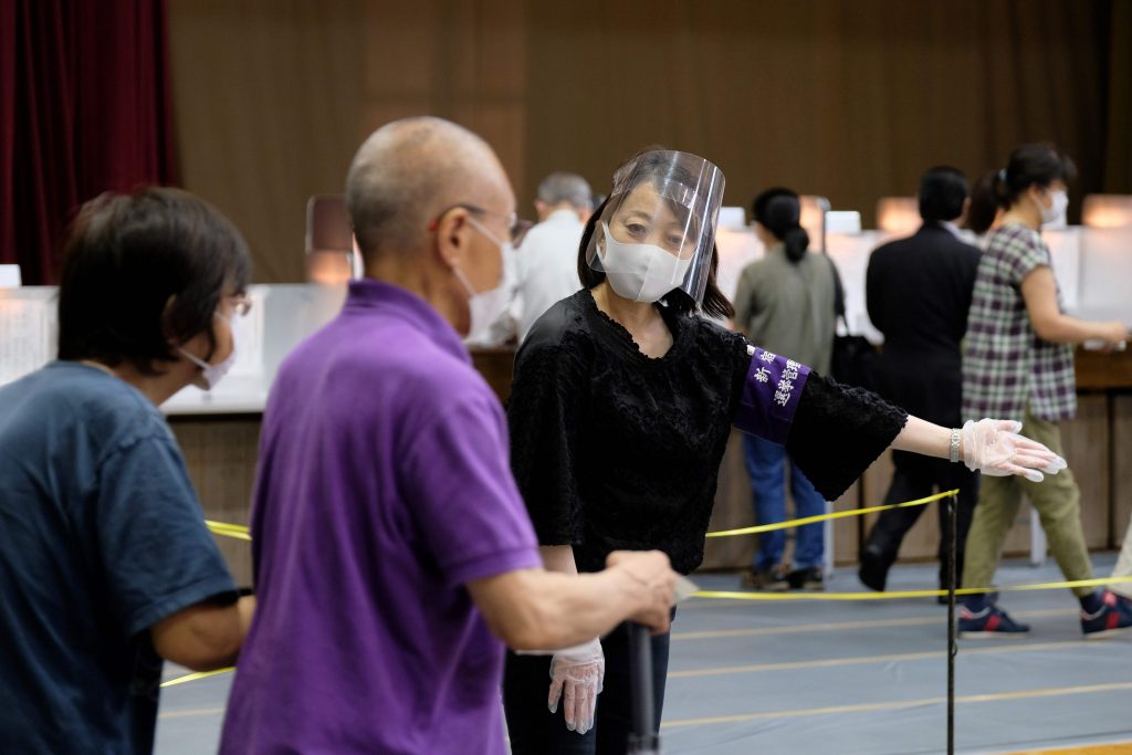 A polling station staff wearing a face mask and a face shield help voters upon their arrival at a polling station for Tokyo gubernatorial election in Shinjuku, Tokyo on July 5, 2020. The postponed Olympics and a worrying second surge in coronavirus cases are the main issues as Tokyo voters vote for governor to run one of the world's most populous cities. (AFP)