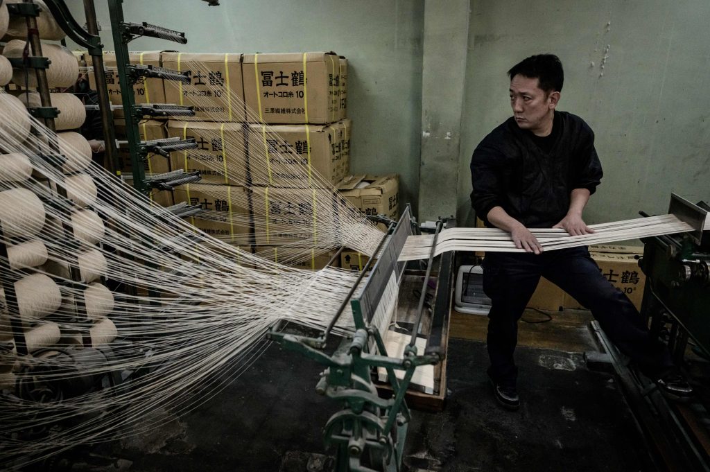 In this picture taken on February 25, 2020, an employee of the Kusakura Japanese martial arts equipment manufacturer checks a vintage weaving machine used for making judo uniform fabric at the factory in Kashiwara, Osaka prefecture. (AFP)