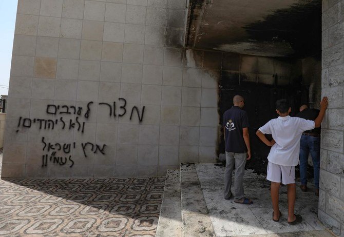 Palestinians inspect the damage at the entrance of a mosque that was torched and sprayed with graffiti in Hebrew. (AFP)