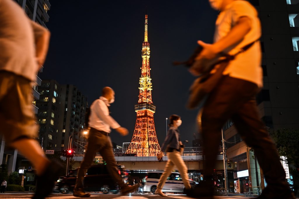 People wearing face masks walk in a street near Tokyo Tower in Tokyo on July 20, 2020. (AFP)