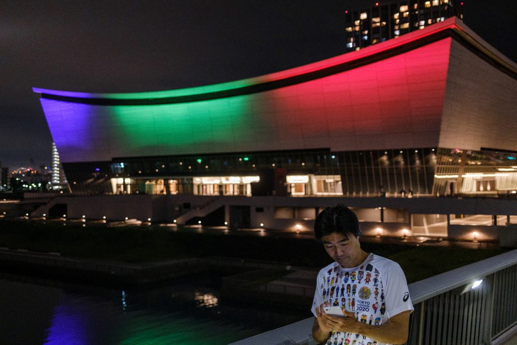 A man looks at his mobile phone in front of the illuminated Ariake Arena, the venue for Olympic volleyball and Paralympic wheelchair basketball, to mark one year until the postponed Tokyo 2020 Olympic and Paralympic Games in Tokyo on July 23, 2020. (AFP)