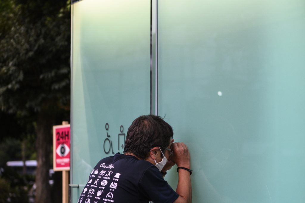 A man attempts to look past opaque glass of an occupied toilet cubicle designed by Shigeru Ban, which its outer walls of transparent glass would turn opaque when the lock is closed, at Haru-no-Ogawa Community Park in the Shibuya district of Tokyo on August 19, 2020. (AFP)