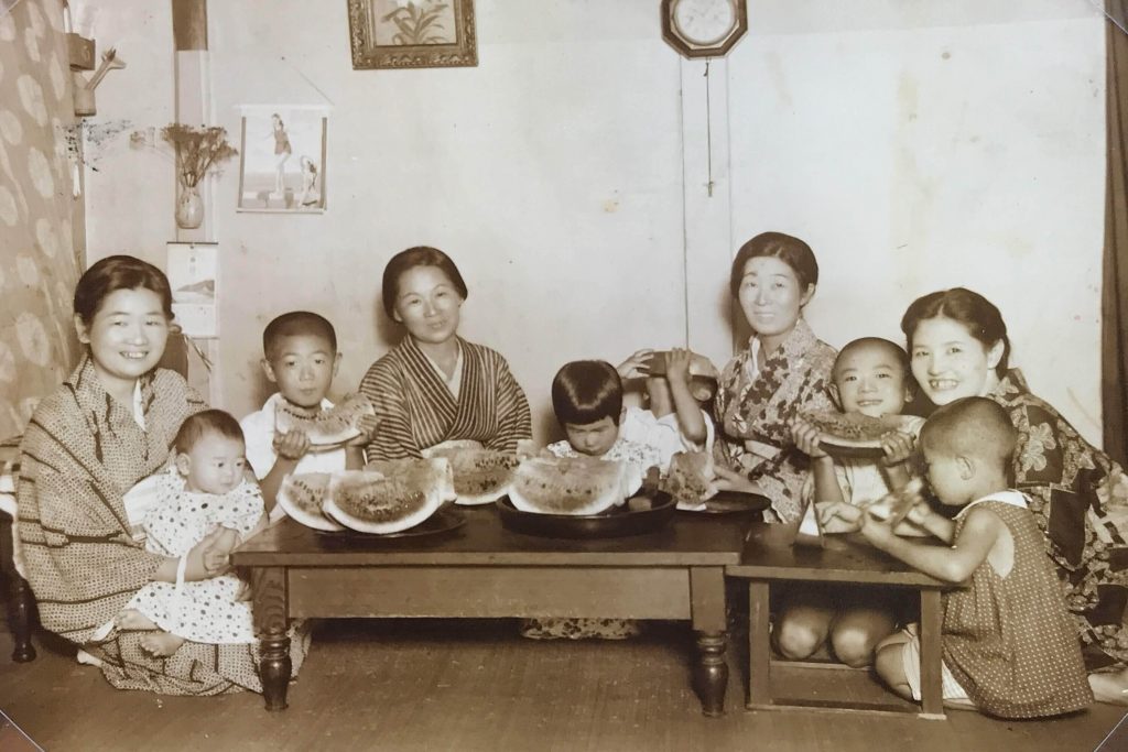 In this black and white photo provided by Hisashi Takahashi and digitally colorized and published in 2020 by Anju Niwata and Hidenori Watanave, Takahashi, covering face with watermelon at center, his family and relatives, pose for a photog eating watermelon around 1932 in Hiroshima, western Japan. (File photo/AP)
