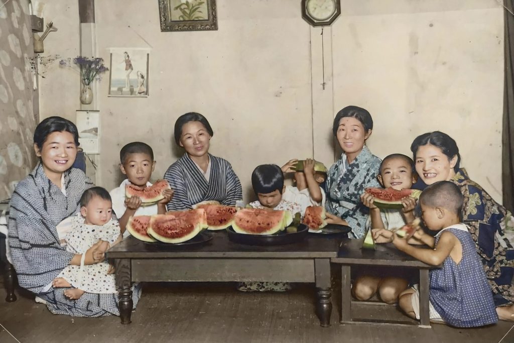 In this black and white photo provided by Hisashi Takahashi and digitally colorized and published in 2020 by Anju Niwata and Hidenori Watanave, Takahashi, covering face with watermelon at center, his family and relatives, pose for a photog eating watermelon around 1932 in Hiroshima, western Japan. (File photo/AP)