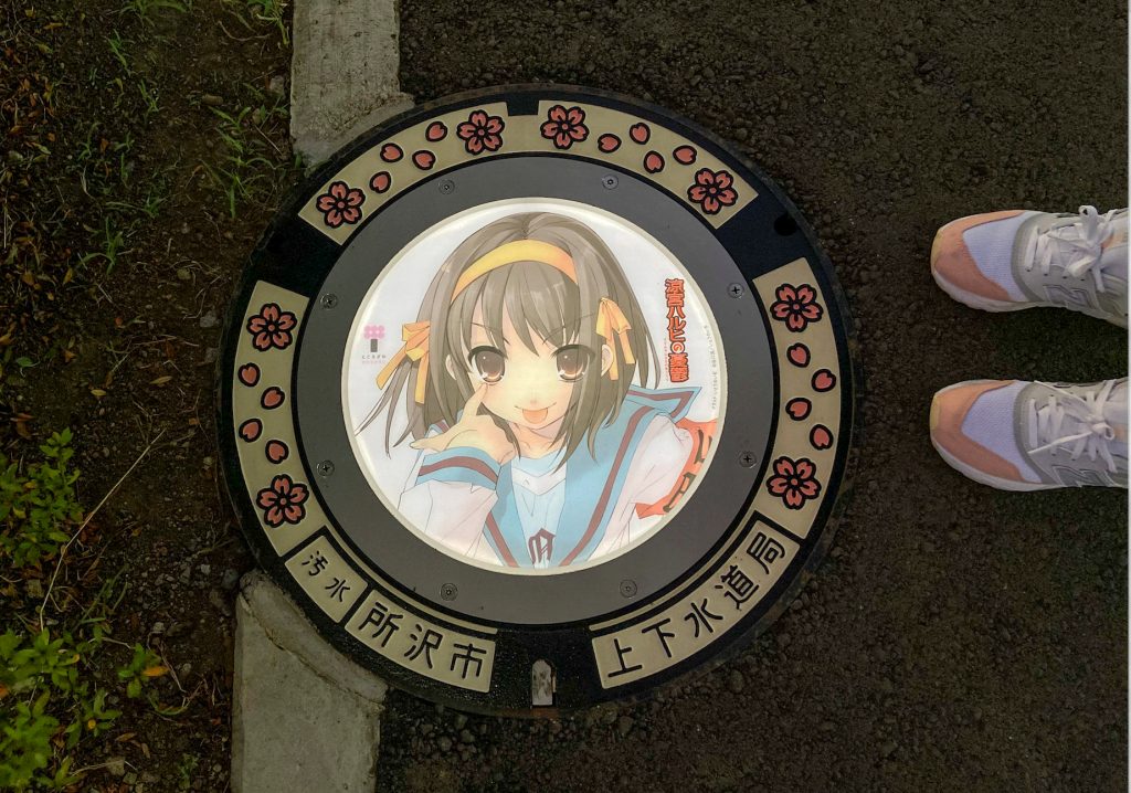 A passerby stands next to an illuminated manhole cover with designs of popular animation character from 'The Melancholy of Haruhi Suzumiya', on the street in Tokorozawa, near Tokyo, Japan August 19, 2020. (Reuters)
