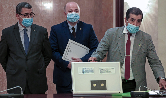A file photo taken on July 04, 2020 shows Algerian Prime Minister Abdelaziz Djerad (L), Finance Minister Aymane Benabderrahmane (C) and Governor of Bank of Algeria (Central Bank) Rosthom Fadli, all wearing protective masks amid the COVID-19 pandemic, presenting samples of new banknotes. (AFP)