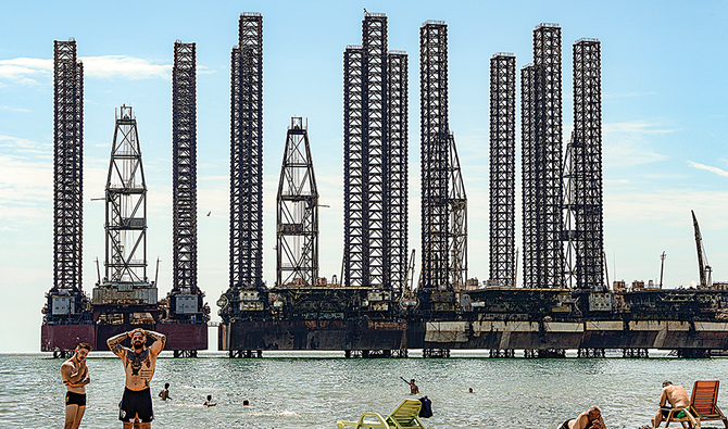 Men rest near oil rigs on a beach in Baku. Top oil companies have slashed oil production rates as the coronavirus pandemic caused a drastic fall in fuel prices. (AFP)