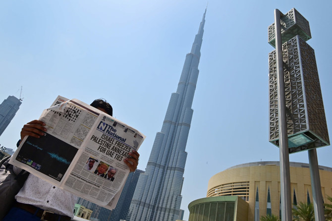 A man reads a copy of UAE-based The National newspaper near the Burj Khalifa in Dubai on August 14, 2020, as the publication's headline reflects the previous day's news as Israel and the UAE agreed to normalize relations in a landmark US-brokered deal. (AFP / Giuseppe Cacace)