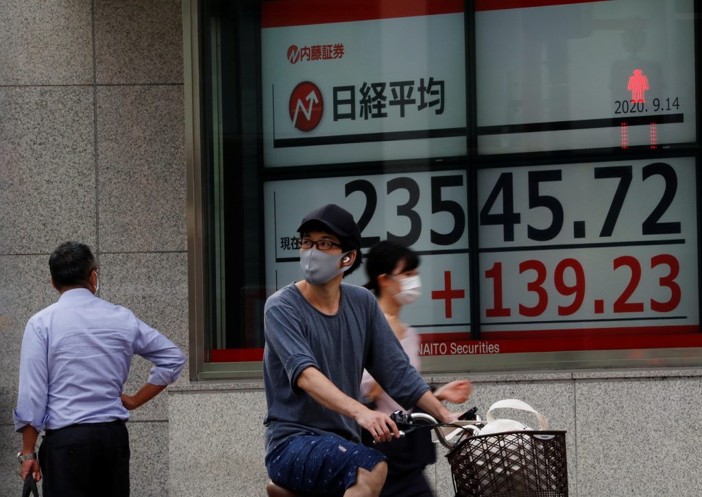 Passersby wearing protective masks walk past an electronic board showing Japan's Nikkei average outside a brokerage, in Tokyo. (File Photo/Reuters)