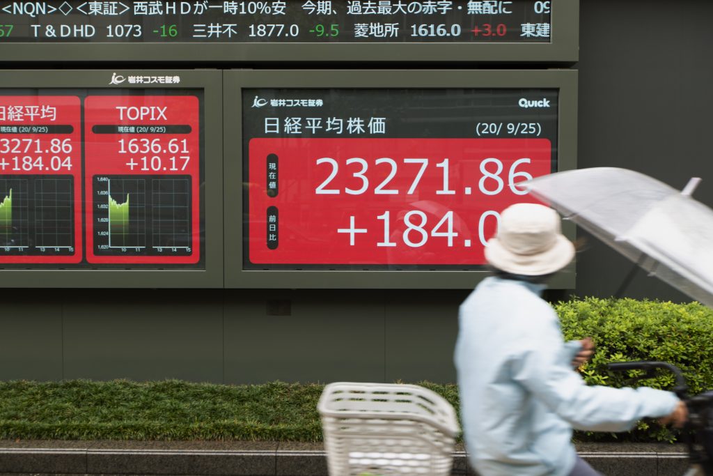 A woman rides a bicycle past screens showing Japan's Nikkei 225 index at a securities firm in Tokyo, Sep. 25, 2020. (File photo/AP)