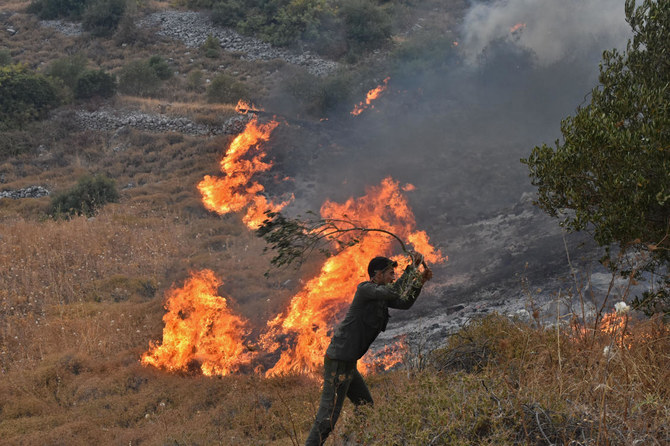 A handout picture released by the official Syrian Arab News Agency (SANA) on September 8, 2020 shows a Syrian man attempting to put off a fire on a hill in Ain Halaqim, in the western countryside of Syria's Hama governorate. (AFP)