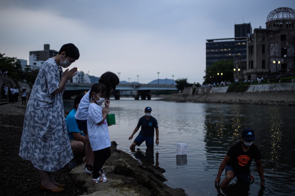 People pray after releasing paper lanterns on Motoyasu River in front of ruins of the Hiroshima Prefectural Industrial Promotion Hall (back R), now commonly known as the atomic bomb dome, in Hiroshima on August 6, 2020. (AFP)