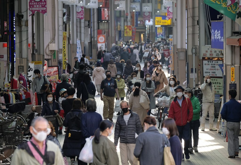 Mask-clad people walk along a street lined with shops in Tokyo, amid concerns of the COVID-19 coronavirus. (AFP)
