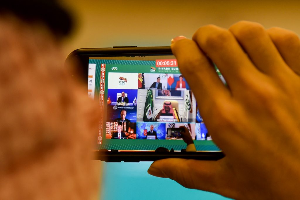 A man uses a phone to film a projected screen at the International Media Centre in Saudi Arabia's capital Riyadh on November 21, 2020 showing Saudi King Salman bin Abdulaziz as he gives an address opening the G20 summit, held virtually due to the COVID-19 coronavirus pandemic, while surrounding him are other G20-participating leaders. (AFP)