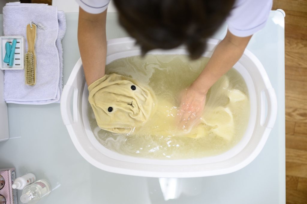 An employee bathing the skin of client Yui Kato's stuffed toy sheep Yuki-chan during a restoration