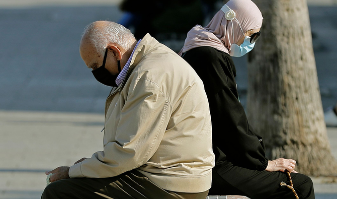 A man and a woman sit back to back on a bench as they enjoy a sunny day near the Beirut seaside promenade on November 24, 2020. (AFP)