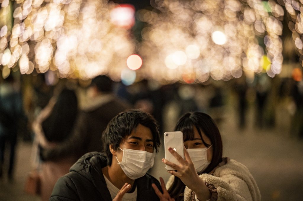 A couple takes pictures in front of Christmas-themed light decorations along a street in Marunouchi district in Tokyo on December 25, 2020. (AFP)