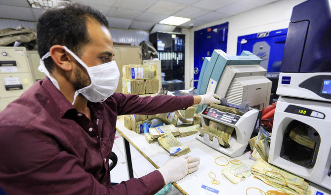 An employee wearing a face mask and gloves counts local currency at a bank in the Yemeni capital Sanaa on March 24, 2020. (AFP)