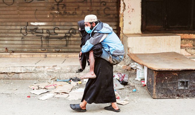 A woman carries a disabled man wearing a protective face mask in the Sabra locality of Beirut, as Lebanon detects the new COVID-19 strain’s first case. (AFP/File)