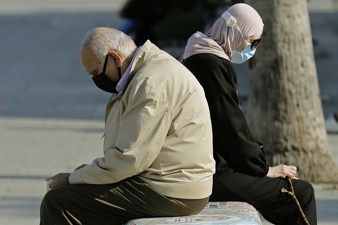 Man and woman sit back to back on a bench as they count worry beads at the Beirut corniche seaside promenade on Nov. 24, 2020. (File/AFP)