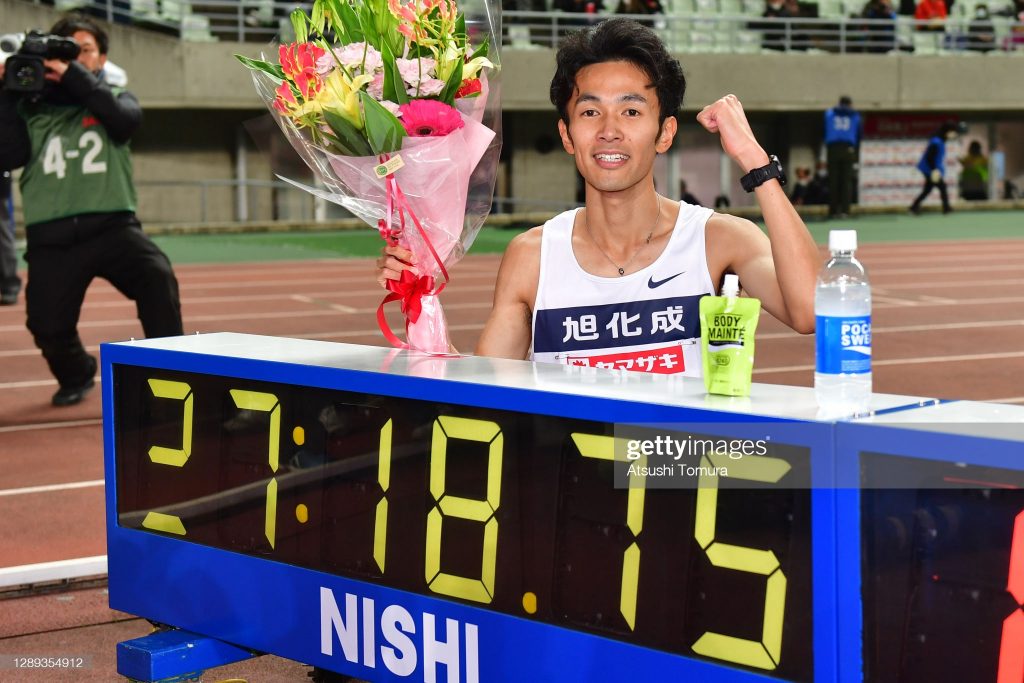 Akira Aizawa poses next to the clock displaying his record time of 27 minutes, 18.75 seconds in the 10,000 meter race.