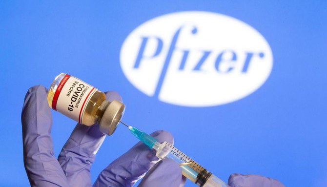 A woman holds a small bottle labeled with a “Coronavirus COVID-19 Vaccine” sticker and a medical syringe in front of displayed Pfizer logo in this illustration taken. (Reuters/file)
