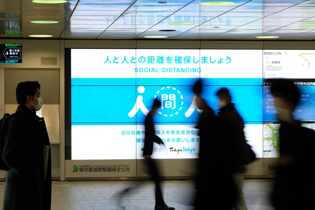 People walk past a public service display promoting social distancing amid the Covid-19 pandemic at a concourse leading to the terminal station in Tokyo's Shinjuku district on January 6, 2021. (AFP)