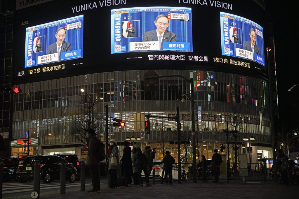 People walk as a public broadcast shows Japanese Prime Minister Yoshihide Suga announcing a state of emergency during a televised news conference in Tokyo, Japan, Jan. 7, 2021. (File photo/EPA)