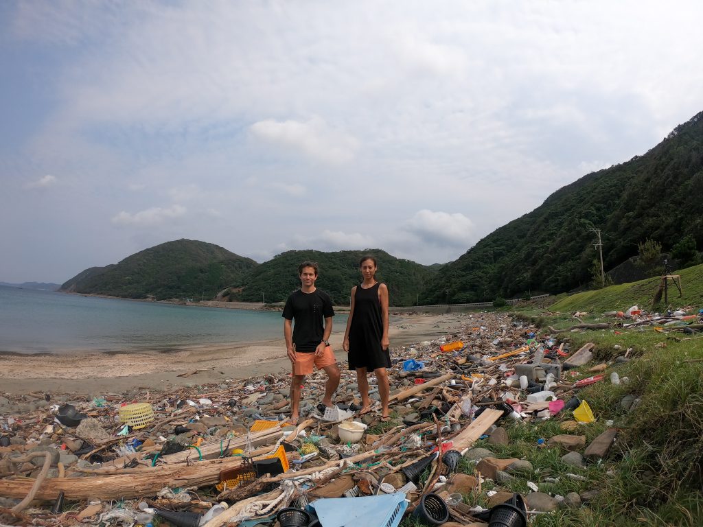 The co-founders of MyMizu Robin Lewis (L) and Mariko McTier (R) are seen standing over plastic waste and other rubbish deposited on a beach. (mymizu/supplied)